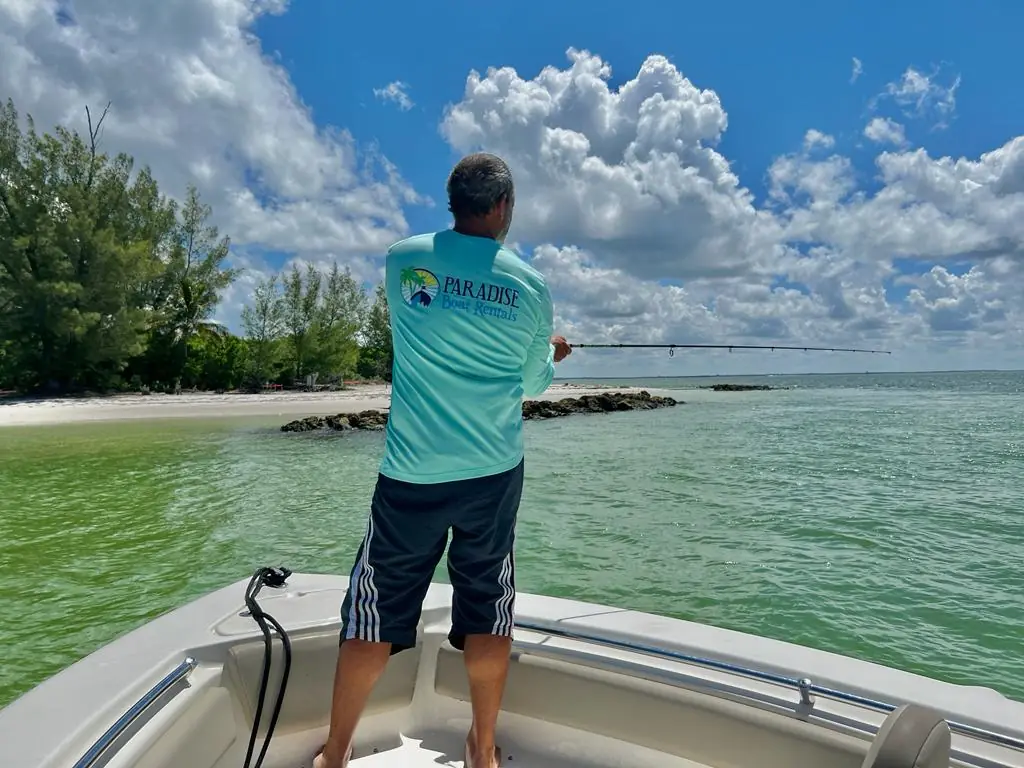 Angler in a Paradise Boat Rentals shirt casting from the bow near an island beach in Southwest Florida